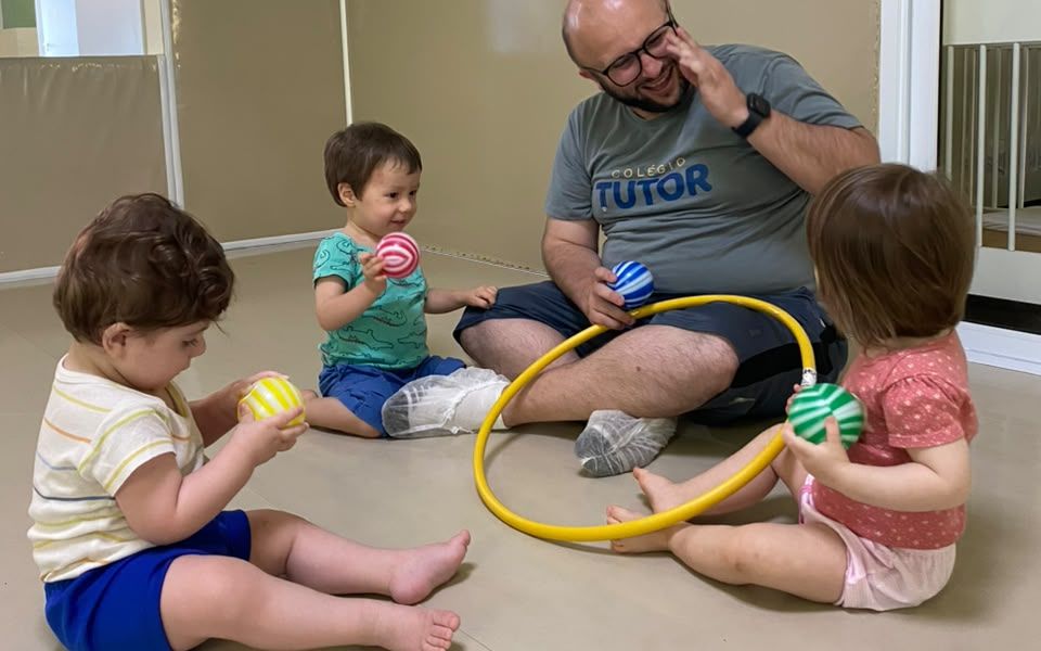 Bebês brincando com bolas e bambolê com o professor no berçário