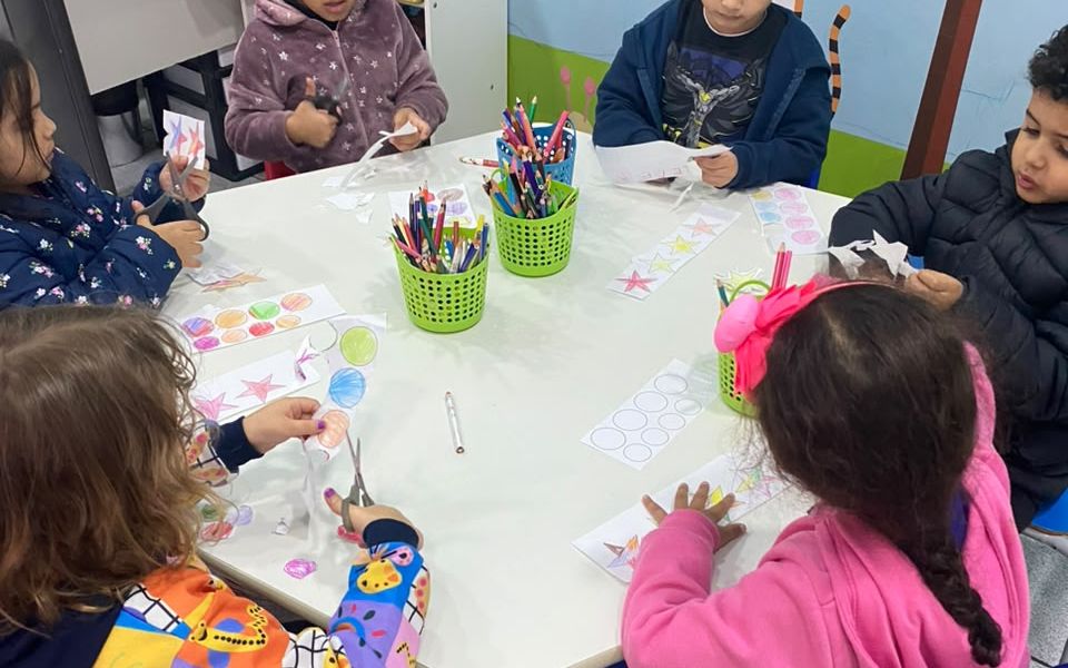 Crianças da Educação Infantil fazendo atividade de recorte em mesa coletiva