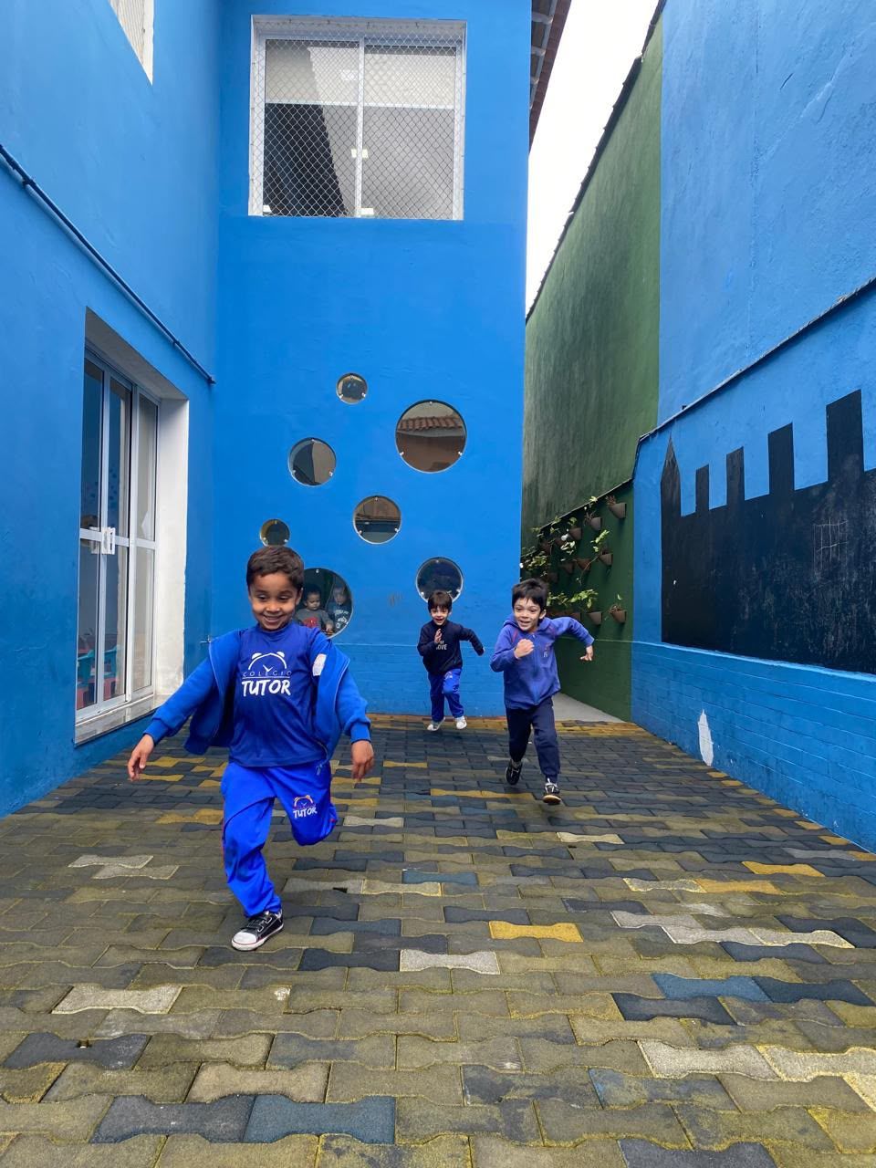 Alunos correndo no pátio azul da escola