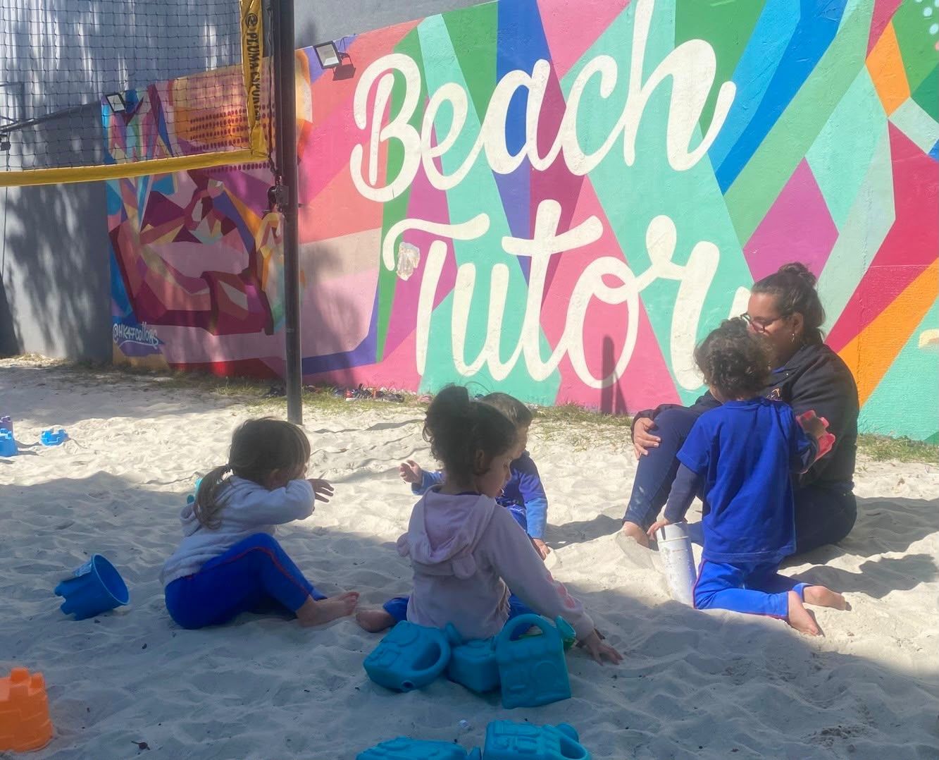 Crianças brincando na areia em frente ao mural Beach Tutor